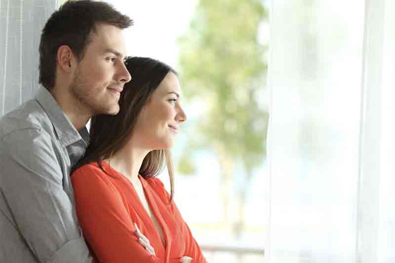 Couple standing together and looking out a window, appearing thoughtful and reflective